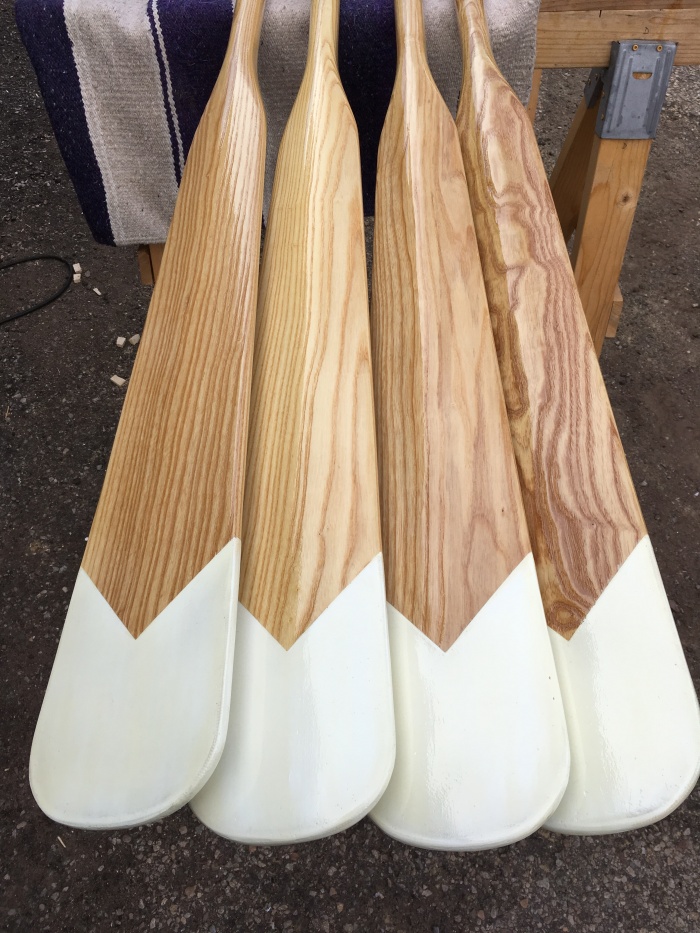 The blades of four wood oars with white chevron designs on their blade tips.