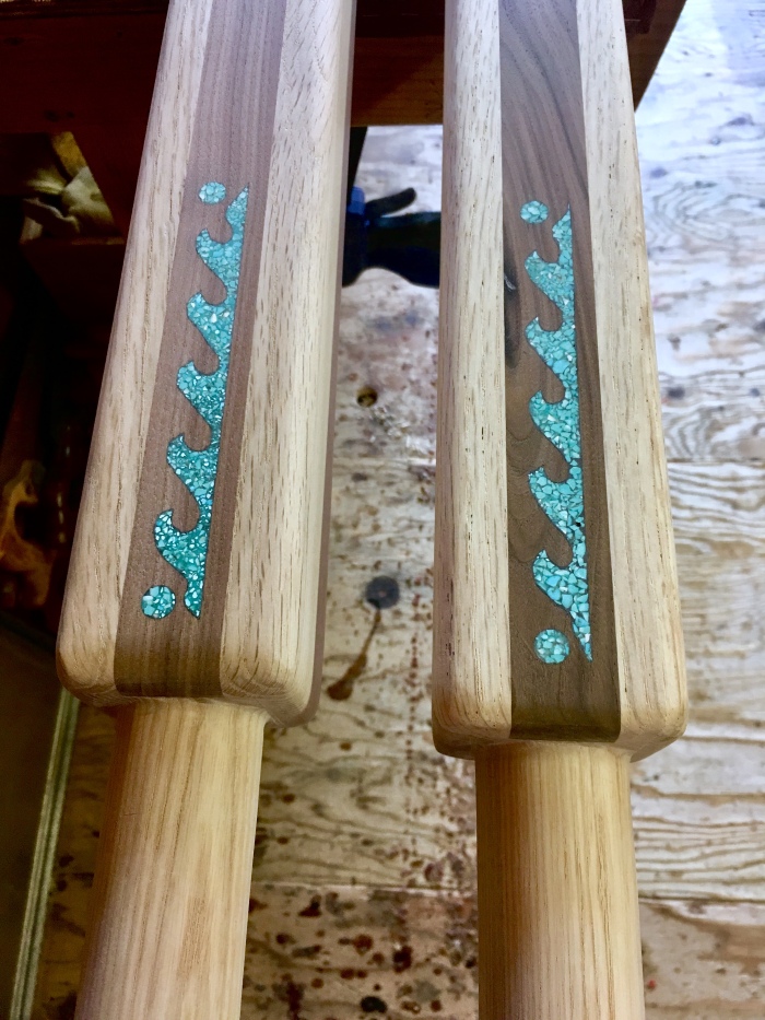 Wooden raft oars made of white ash, Sierra black oak, and walnut. The square shaped inboard portion of the oars is inlaid with turquoise in the shape of the waves of a river rapid with the sun and moon on each side.
