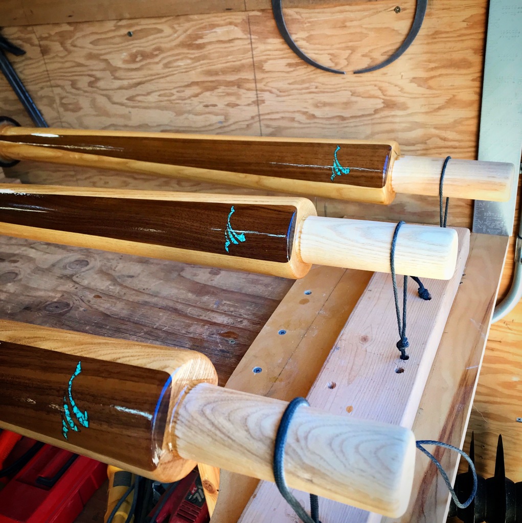 Three oars custom made for a Colorado River guide with inlaid turquoise wave motifs drying in the oar-shop after being varnished.